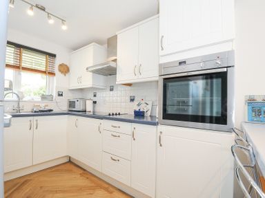 A kitchen with white cabinets a built-in oven a microwave a window with wooden blinds and a sink at Slipway 16 in Rock