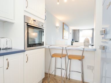 A kitchen area with white cabinets a built-in oven a toaster and two bar stools at Slipway 16 in Rock