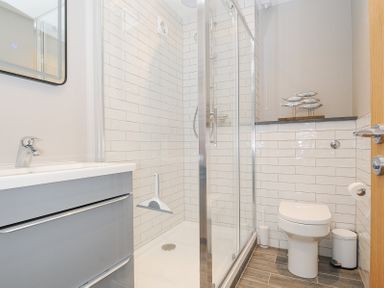 A bathroom with a shower enclosure a toilet a sink with cabinet and fish decoration on a shelf at Slipway 16 in Rock