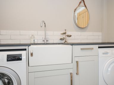 A laundry room with a washing machine, dryer, sink, and mirror at Slipway 16 in Rock