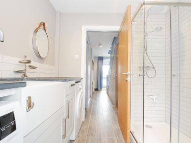 A bathroom with a shower cabin washing machine and a round mirror at Slipway 16 in Rock