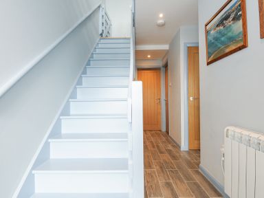 A white staircase leading up with wooden doors and framed pictures on the walls in a hallway at Slipway 16 in Rock