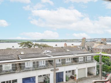 A balcony railing overlooking rooftops with water and green hills in the background at Slipway 16 in Rock
