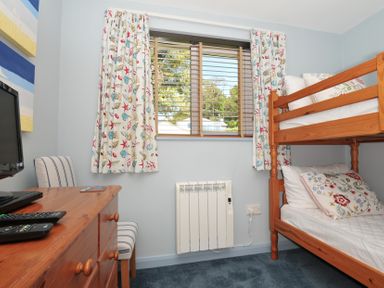 A bedroom with a bunk bed curtains with shell patterns a wooden dresser and a chair at Slipway 16 in Rock
