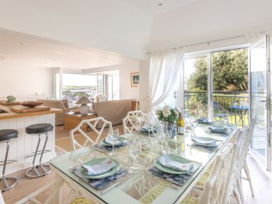 A dining area with glass table set for six and chairs next to a balcony and an open living room with sofas at Slipway 19 in Rock