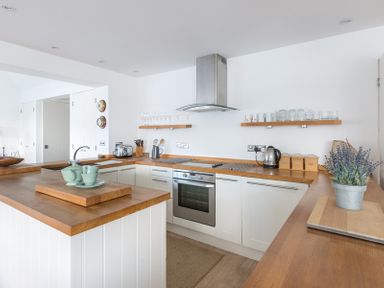 A kitchen with wooden countertops white cabinets a stove and kitchen utensils at Slipway 19 in Rock