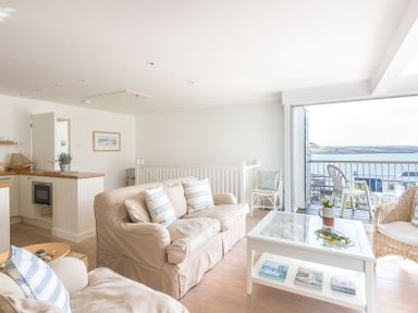 A living room with beige sofas blue striped cushions a white coffee table and a balcony with chairs overlooking the sea at Slipway 19 in Rock