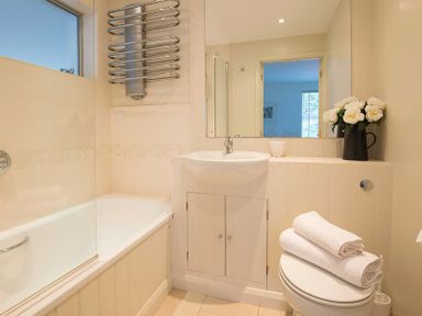 A bathroom with a bathtub shower combination a sink a toilet with towels and a vase of flowers at Slipway 19 in Rock