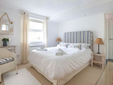 A bedroom with a double bed with striped headboard bedside tables with lamps a chair and a window at Slipway 19 in Rock