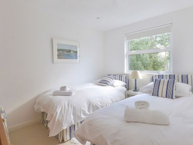 A bedroom with two single beds with striped headboards and pillows a lamp on a bedside table and a window at Slipway 19 in Rock