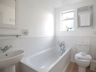 A bathroom with a bathtub sink toilet heated towel rail and window at Slipway 19 in Rock