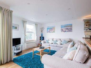 A living room with two beige sofas and blue cushions a blue rug a glass TV stand with a TV and a wooden coffee table at Slipway 21 in Rock