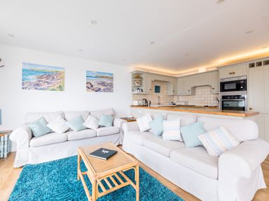 A living room with two white sofas and a wooden coffee table on a blue rug next to a kitchen with beige cabinets at Slipway 21 in Rock