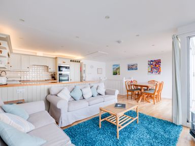 An open living room with two sofas and a blue rug next to a kitchen with white cabinets and wooden dining table with chairs at Slipway 21 Rock