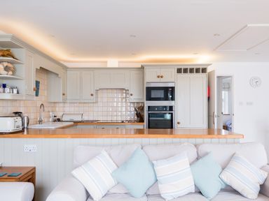 A kitchen with cabinets appliances and a wooden countertop behind a sofa with cushions at Slipway 21 in Rock