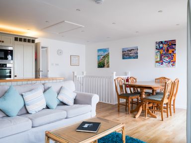 A living area with a sofa and cushions a wooden dining table with chairs and paintings on the walls at Slipway 21 in Rock