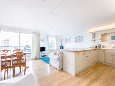 An open plan kitchen and living area with wooden dining table and chairs a sofa and TV at Slipway 21 in Rock
