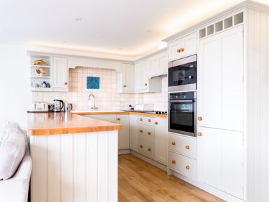 A kitchen with white cabinets wooden countertop built in oven and microwave and a tiled backsplash at Slipway 21 in Rock