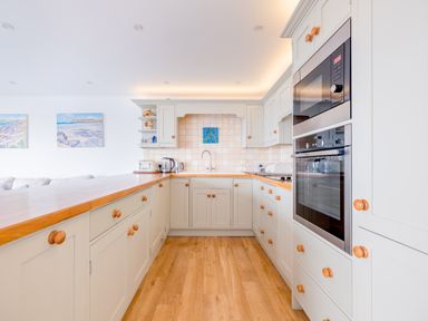 A kitchen with white cabinets wooden knobs a wooden countertop and built in appliances at Slipway 21 in Rock