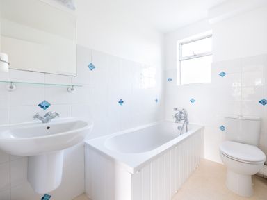 A bathroom with a sink, bathtub, toilet, and window with white tiled walls at Slipway 21 in Rock