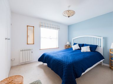 A bedroom with a blue bedspread on a bed with a white headboard two bedside tables with lamps a window with a striped blind and a wall mirror at Slipway 21 in Rock