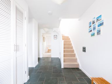 A hallway with slate tile floor and beige carpeted stairs with photo frames on the wall at Slipway 21 in Rock