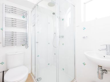 A bathroom with a toilet a glass-enclosed shower a sink and a chrome towel radiator at Slipway 21 in Rock