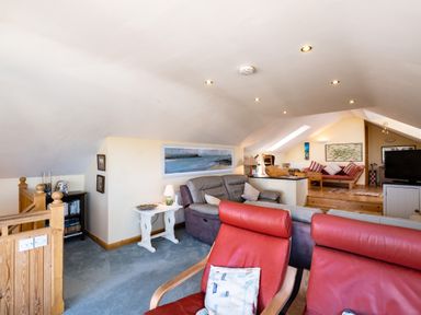 A living room with sofas red armchairs a wooden bookcase and a television at Little Belz in Polzeath