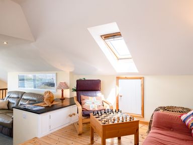A loft room with a leather armchair a sofa a chess table a wicker ottoman and a skylight at Little Belz in Polzeath