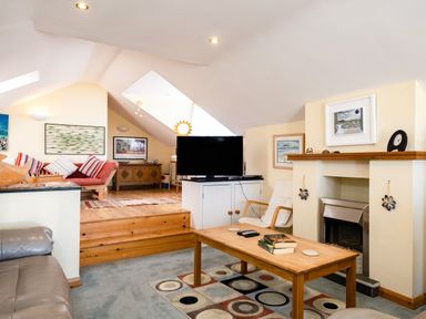 A living room with a wooden coffee table, television, fireplace, and a pink couch with striped pillows at Little Belz in Polzeath