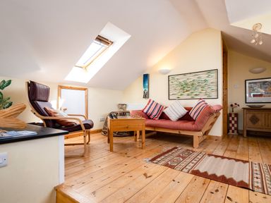 A sitting area with a wooden chair and a sofa with striped cushions under a skylight at Little Belz in Polzeath