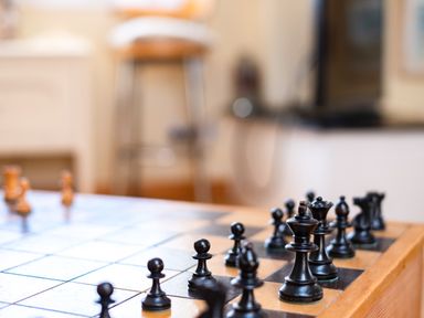 A chessboard with black chess pieces arranged on a wooden table in a room with blurred furniture in the background at Little Belz in Polzeath