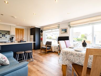 A kitchen and dining area with stools chairs a dining table and windows at Little Belz in Polzeath