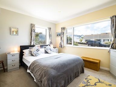 A bedroom with a bed bedside tables windows and a yellow rug at Little Belz in Polzeath