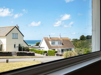 A view of two houses with hedges a road and the sea in the background taken from inside a building