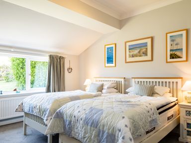 A bedroom with two single beds with quilts and pillows two bedside tables with lamps and three framed pictures on the wall at Little Belz in Polzeath