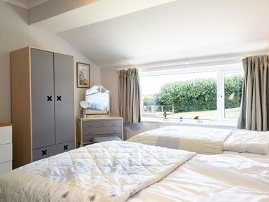 A bedroom with two beds a wardrobe a dresser with mirror and a window with curtains at Little Belz in Polzeath