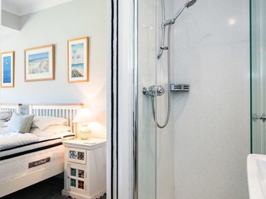 A bedroom with two single beds and a bedside table with a lamp next to a shower with glass doors at Little Belz in Polzeath