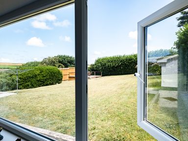 A view of a grass lawn with bushes and a clothes drying rack seen through an open window at Little Belz in Polzeath