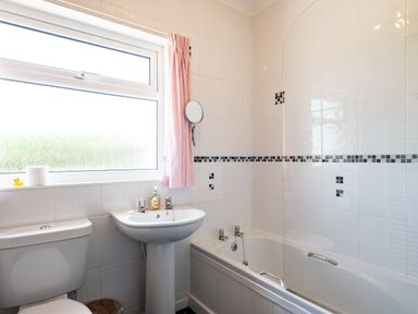 A bathroom with a toilet sink bathtub and a window with pink curtain at Little Belz in Polzeath