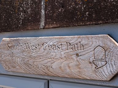 A wooden sign carved with South West Coast Path directions and distances on a wall