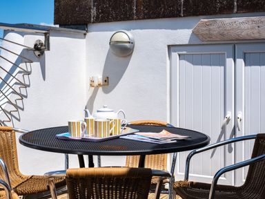 An outdoor patio table with cups teapot and magazines surrounded by chairs at Little Belz in Polzeath