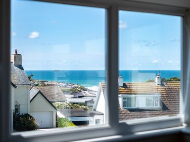 A window view showing rooftops and the sea with blue sky at Little Belz in Polzeath