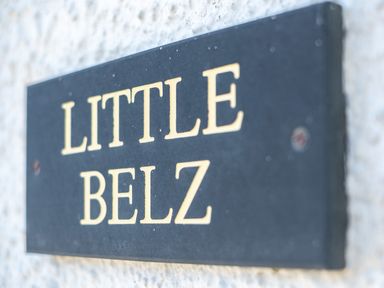 A close up view of a dark rectangular plaque with the text LITTLE BELZ mounted on a white textured surface at Little Belz in Polzeath