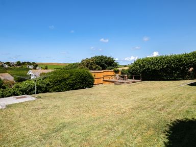 A grassy backyard with a patio drying rack and wooden deck with chairs and table at Little Belz in Polzeath