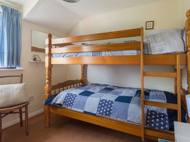 A bedroom with a wooden bunk bed a wooden chair with a cushion and a window with blue check curtains at Hazelhurst in Rock