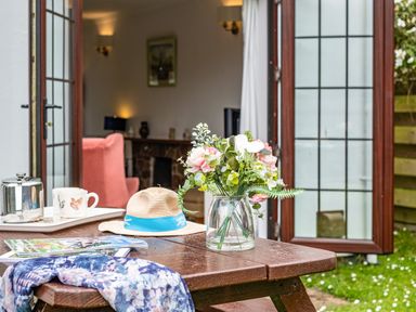 A garden table with a vase of flowers a hat a scarf and a tray with a teapot and mugs outside open doors to a living room at Hazelhurst in Rock