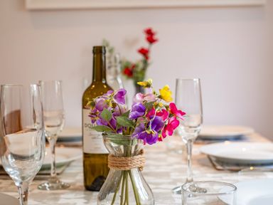 A dining table with a glass vase of colorful flowers wine bottle empty wine glasses and white plates at Hazelhurst in Rock