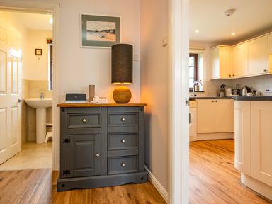 A hallway with a grey cabinet holding a lamp and electronic devices next to a bathroom and kitchen at Hazelhurst Rock