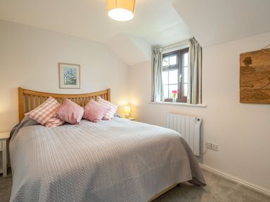 A bedroom with a bed with pink pillows and a gray bedspread a window with striped curtains and a bedside lamp at Hazelhurst in Rock